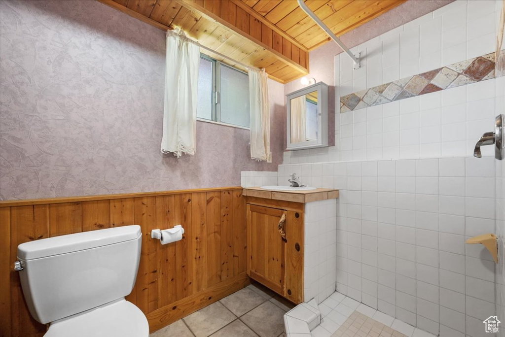 Bathroom with wood ceiling, tile patterned floors, a sink, toilet, and wainscoting