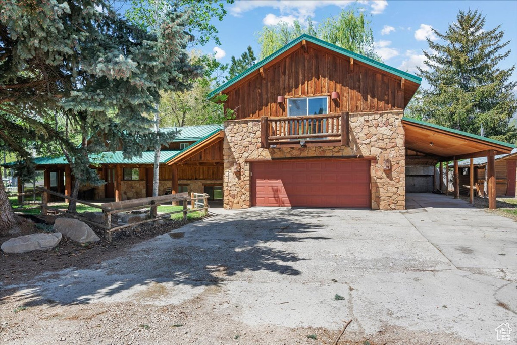Rustic home featuring stone siding, board and batten siding, driveway, and a carport