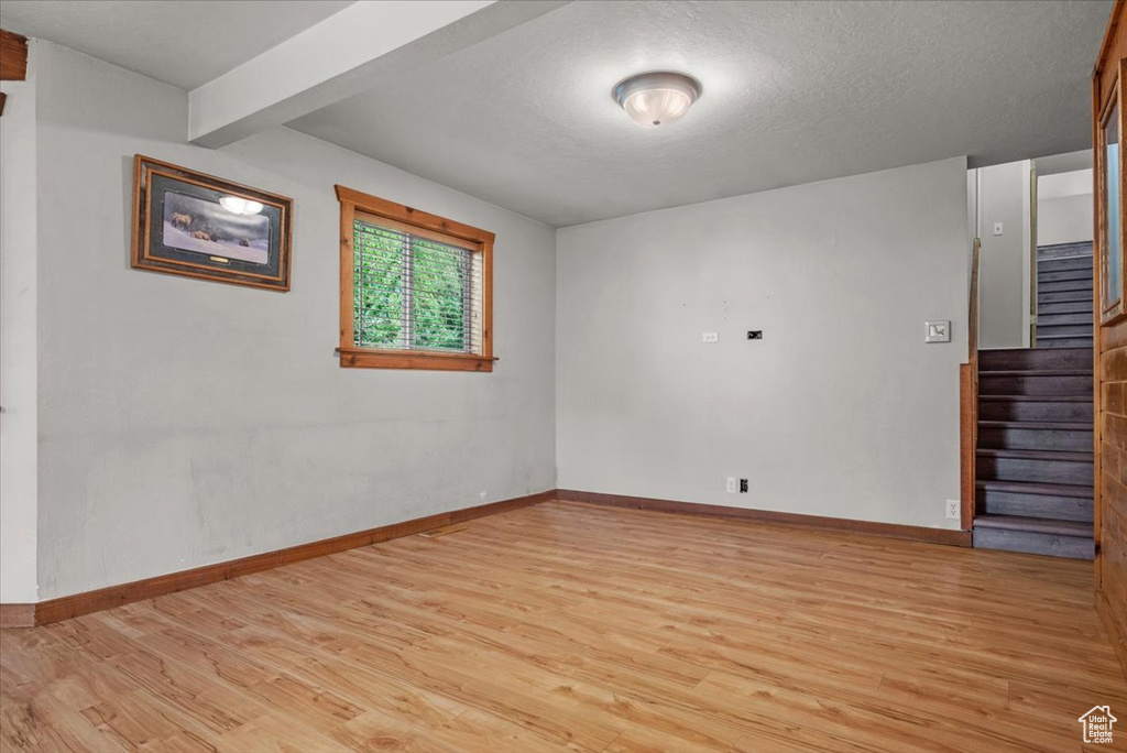 Unfurnished room featuring light wood-style flooring, stairs, baseboards, a textured ceiling, and beam ceiling