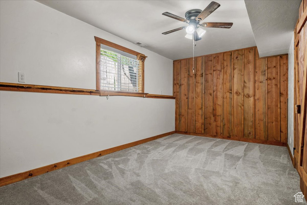 Empty room featuring carpet floors, wooden walls, ceiling fan, and baseboards