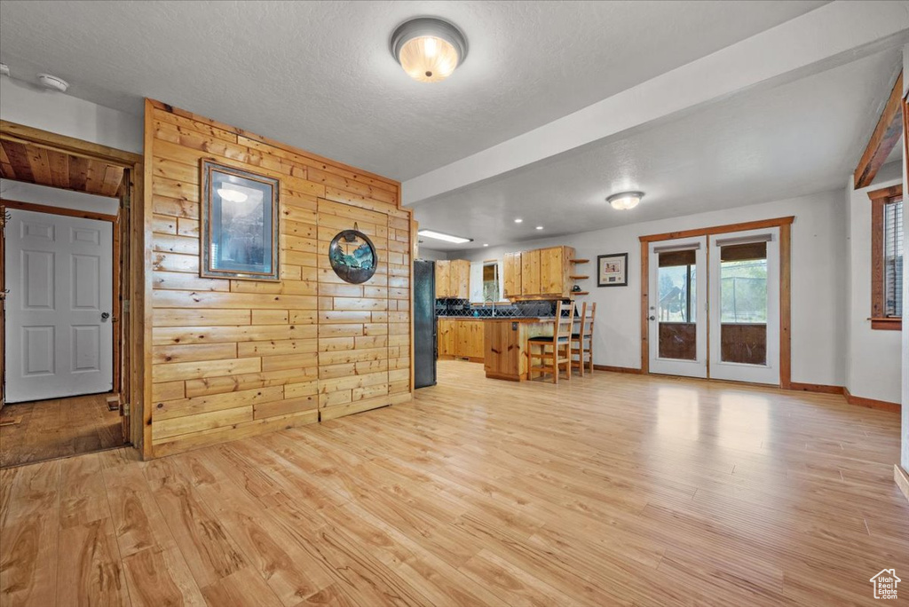 Living area featuring light wood-type flooring, wood walls, baseboards, and french doors