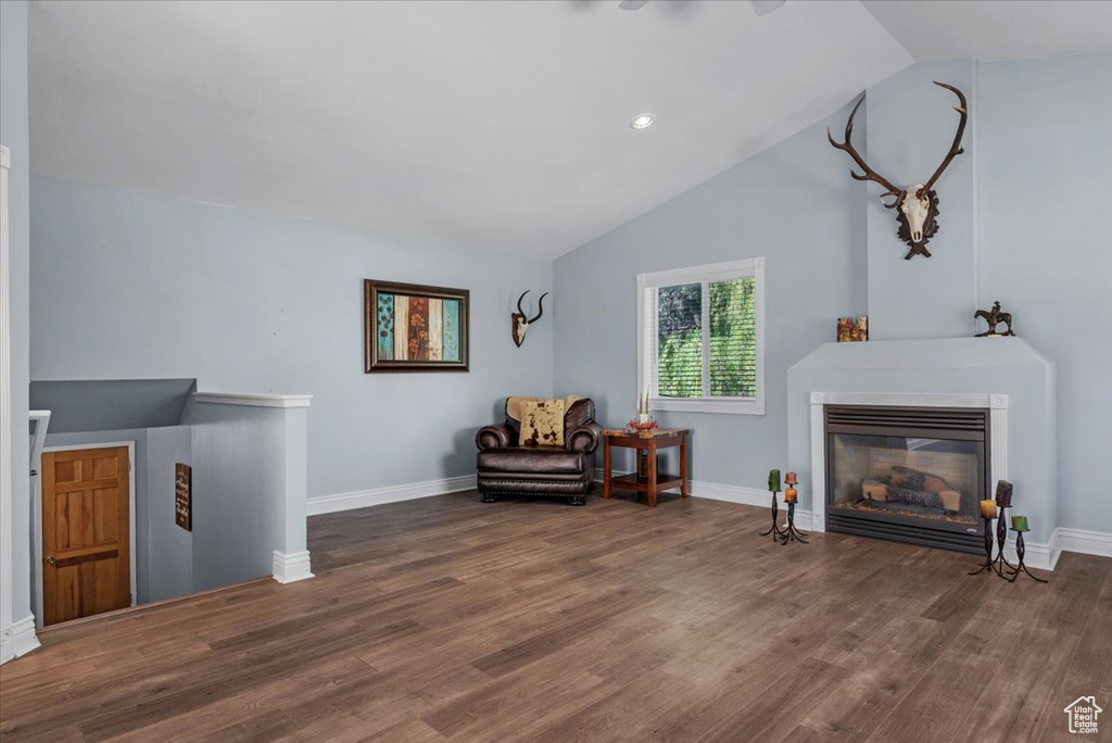 Living area with vaulted ceiling, wood finished floors, an upstairs landing, baseboards, and a glass covered fireplace