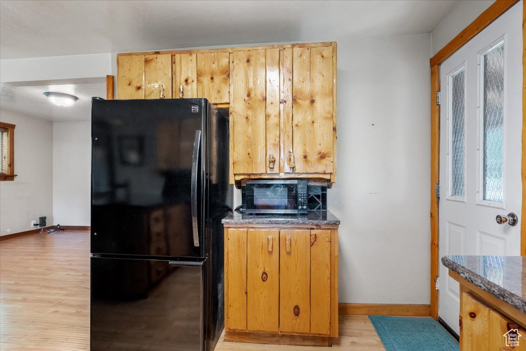Kitchen featuring freestanding refrigerator, stainless steel microwave, light wood-style floors, baseboards, and dark stone countertops