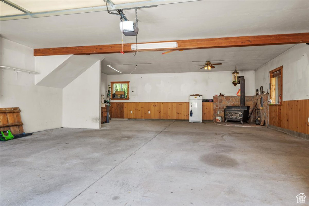 Garage featuring wood walls, a garage door opener, wainscoting, and a wood stove