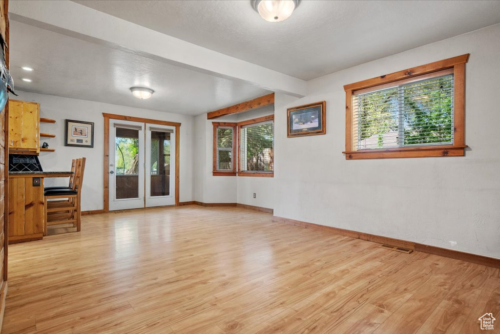 Empty room with baseboards, light wood-type flooring, beam ceiling, and french doors