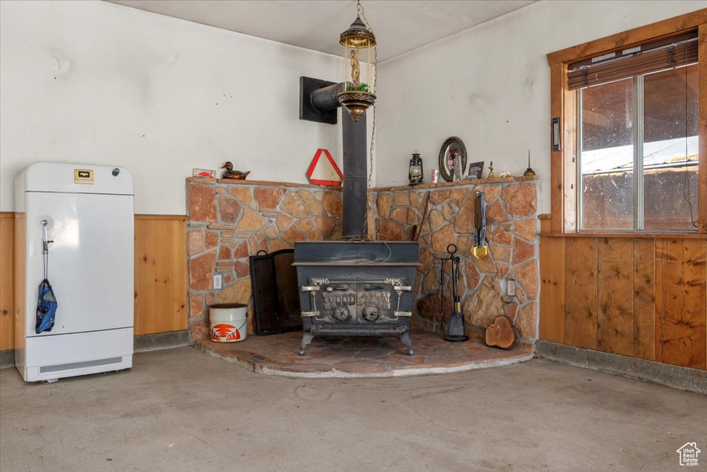 Living room featuring a wood stove, concrete flooring, wooden walls, and wainscoting