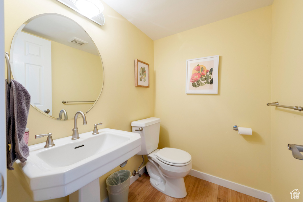 Half bathroom featuring toilet, wood finished floors, baseboards, and a sink