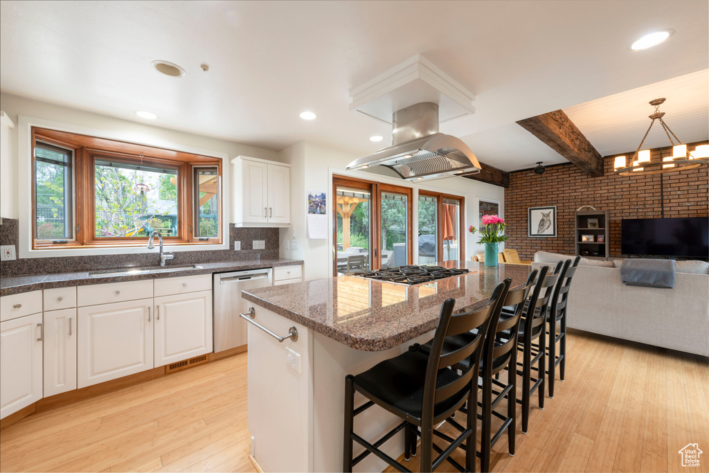 Kitchen featuring appliances with stainless steel finishes, a sink, island exhaust hood, light wood finished floors, and a kitchen island