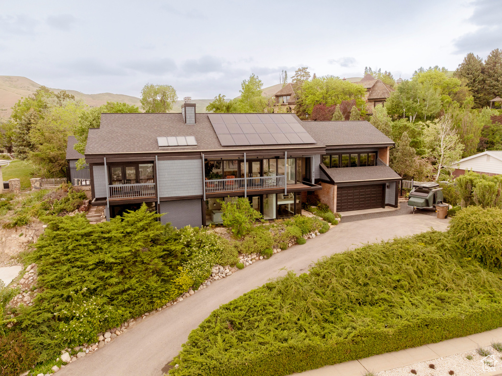 View of front facade with solar panels, an attached garage, a chimney, driveway, and roof with shingles