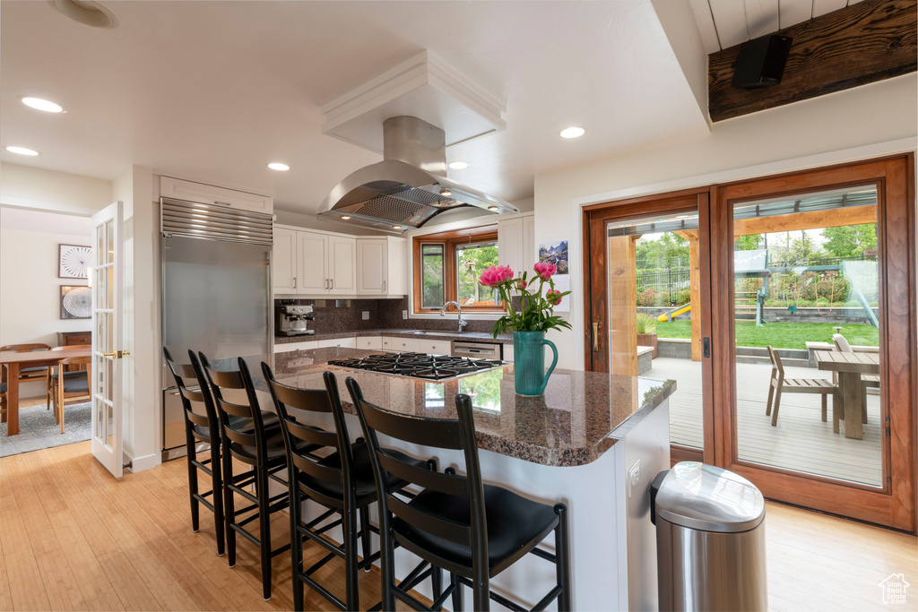 Kitchen with island range hood, stainless steel appliances, a sink, light wood-style floors, and recessed lighting