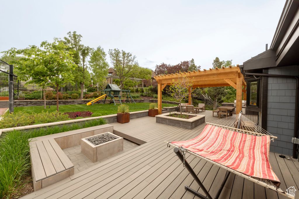 Deck with a playground, fence, a pergola, and an outdoor fire pit