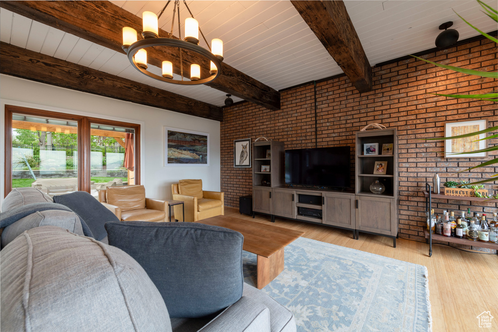 Living area with brick wall, a chandelier, beamed ceiling, light wood-style flooring, and wood ceiling