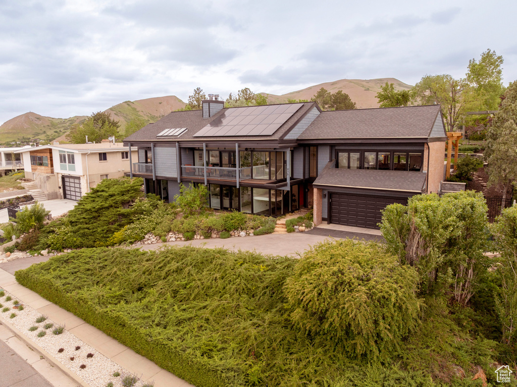 Back of house with a mountain view, roof mounted solar panels, a balcony, a chimney, and driveway