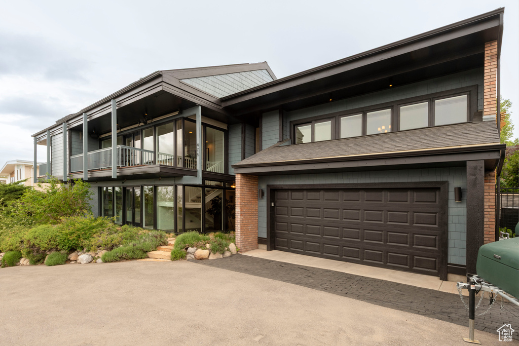 View of front of home featuring asphalt driveway, a balcony, brick siding, and a garage