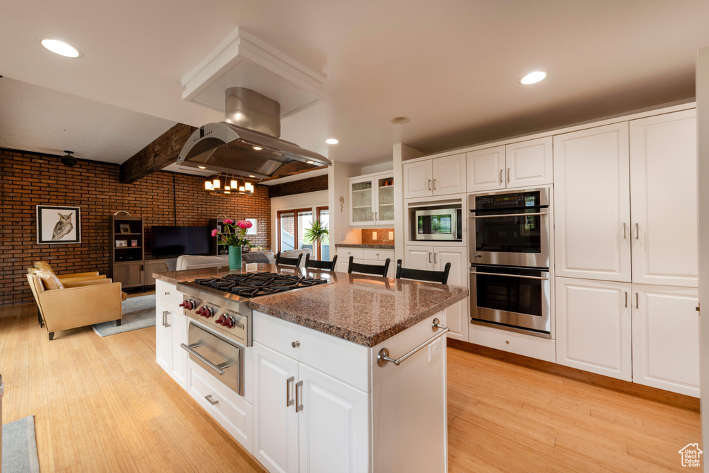 Kitchen with appliances with stainless steel finishes, island range hood, light wood-style flooring, brick wall, and a center island