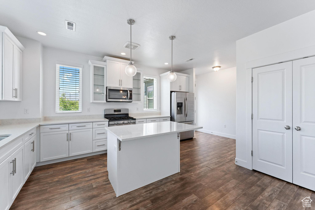 Kitchen with stainless steel appliances, dark wood-type flooring, a center island, white cabinetry, and light countertops