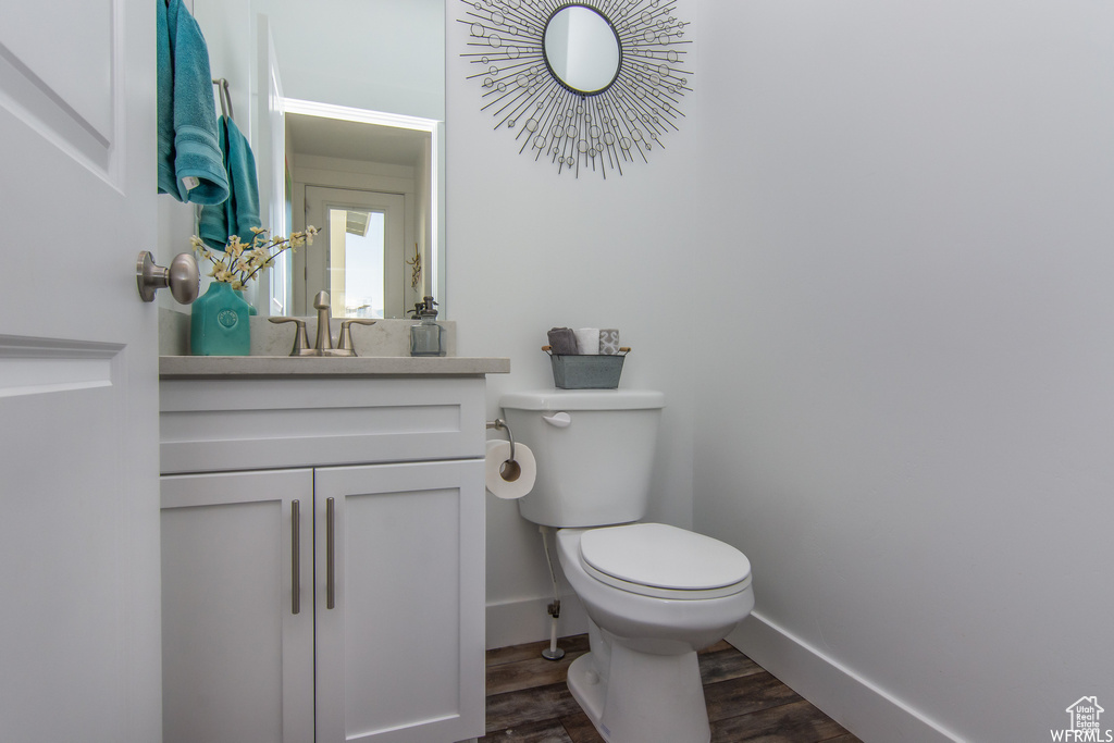 Bathroom featuring wood finished floors, toilet, baseboards, and vanity