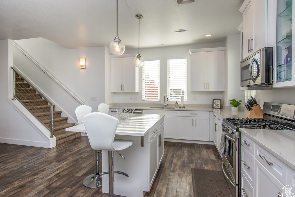 Kitchen with stainless steel appliances, a breakfast bar area, a sink, dark wood finished floors, and light countertops