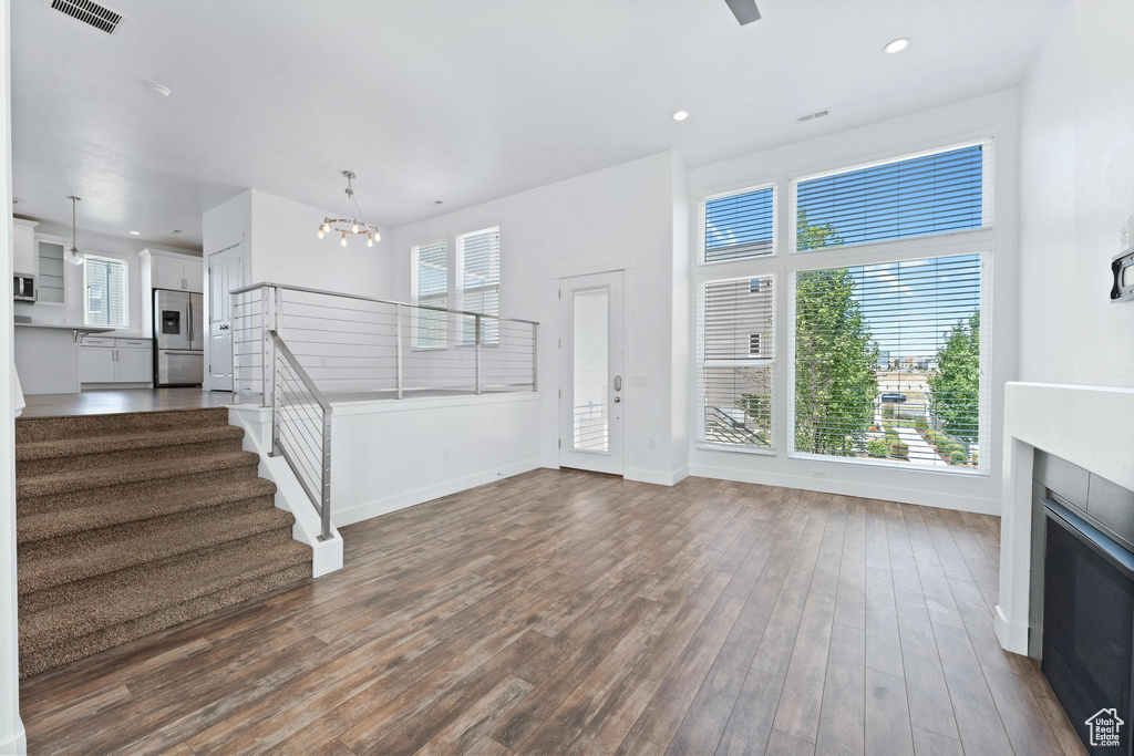 Unfurnished living room with plenty of natural light, stairway, dark wood-type flooring, a chandelier, and recessed lighting