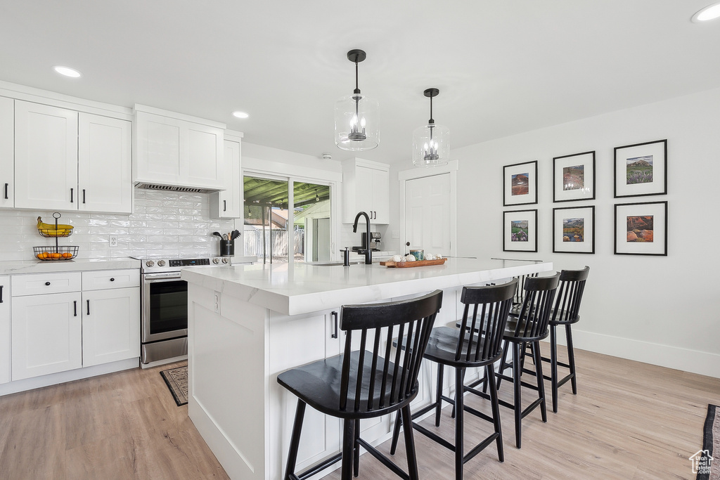 Kitchen with stainless steel electric stove, a sink, baseboards, light countertops, and backsplash