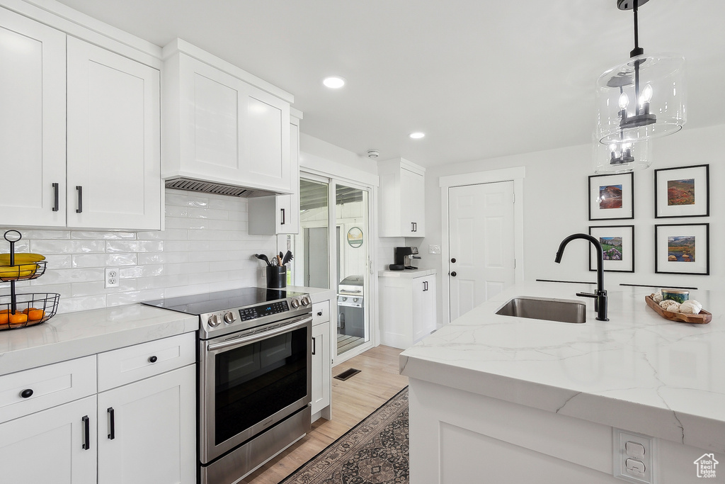 Kitchen with electric range, a sink, white cabinetry, light wood-style floors, and recessed lighting