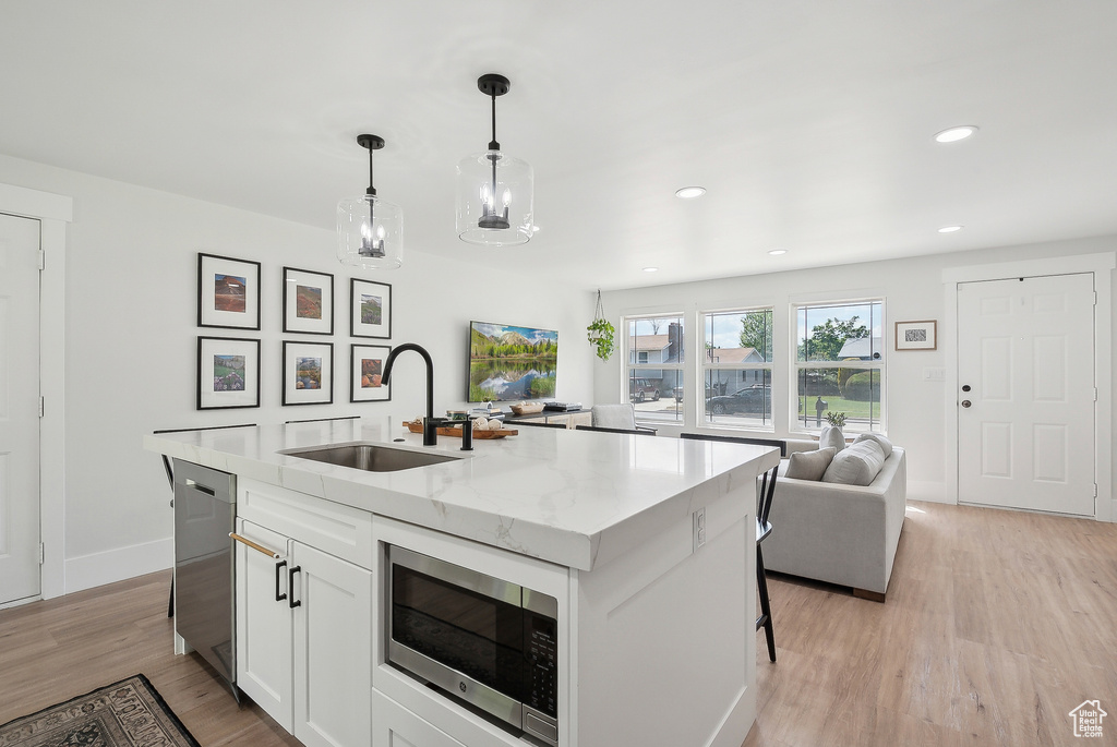 Kitchen featuring a sink, stainless steel appliances, white cabinets, light wood-style floors, and a kitchen island with sink