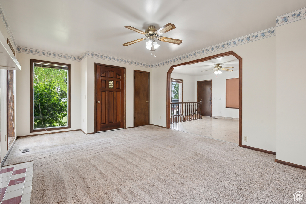 Carpeted foyer entrance featuring ceiling fan, baseboards, and arched walkways