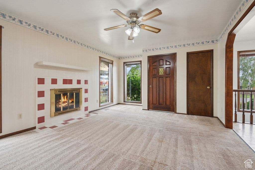 Unfurnished living room with carpet flooring, a ceiling fan, a tile fireplace, and baseboards