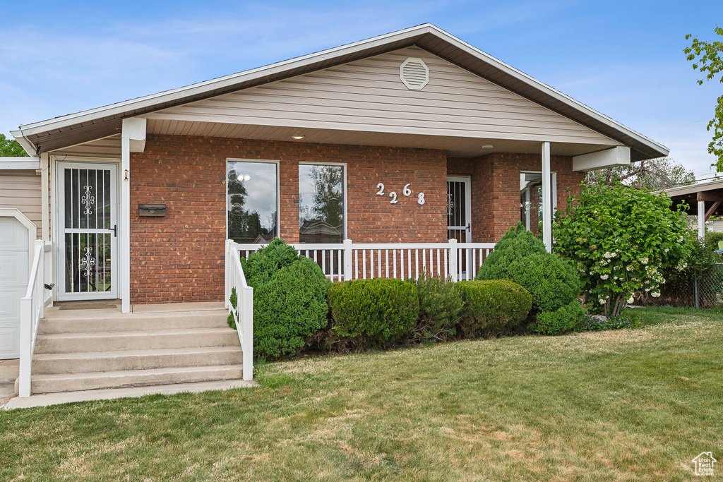 View of front of home with a front yard, brick siding, and covered porch