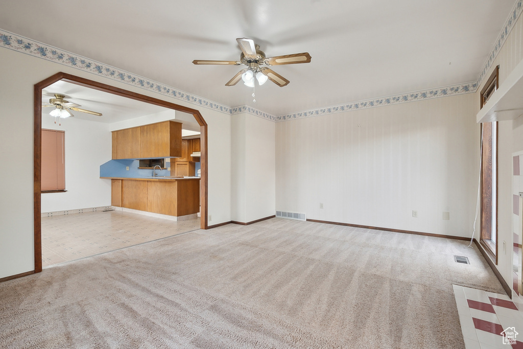 Unfurnished living room featuring a ceiling fan, carpet flooring, and baseboards