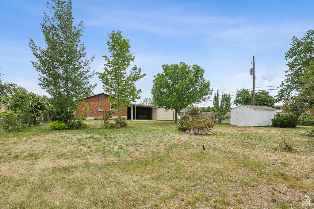 View of green lawn with a storage unit, a sunroom, and an outdoor structure