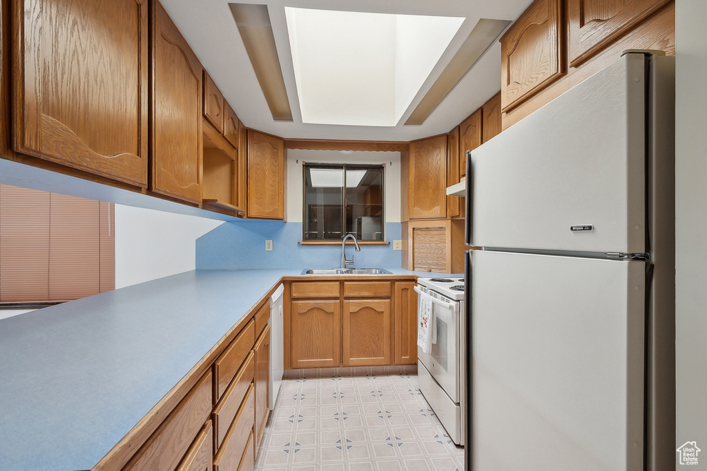 Kitchen with white appliances, a sink, light floors, light countertops, and brown cabinetry