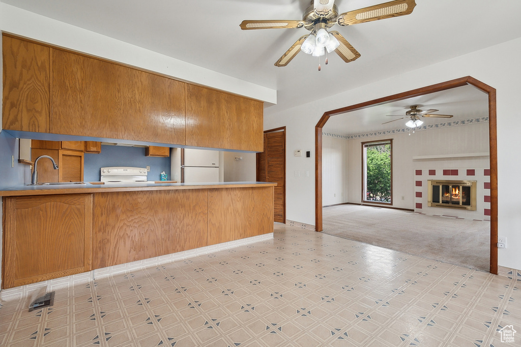 Kitchen featuring ceiling fan, white appliances, light floors, brown cabinets, and a sink