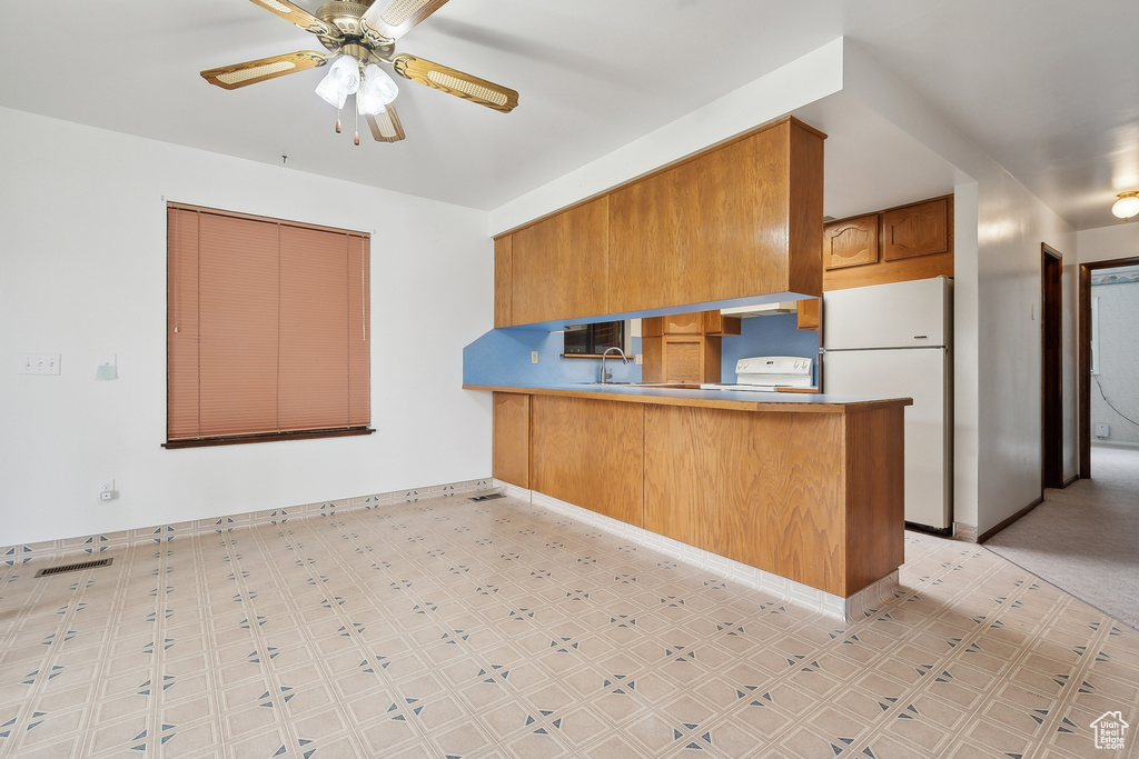 Kitchen with freestanding refrigerator, a peninsula, light floors, brown cabinetry, and a ceiling fan