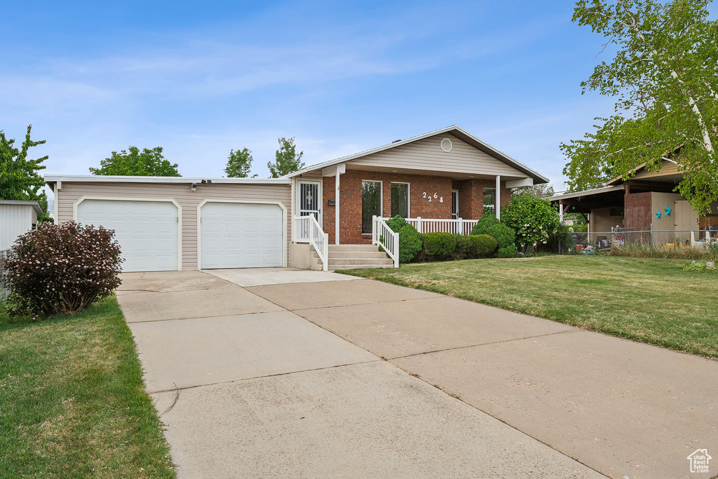 Single story home with a garage, concrete driveway, a front yard, covered porch, and brick siding