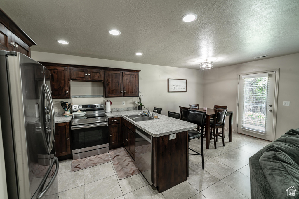 Kitchen with stainless steel appliances, a peninsula, light countertops, a textured ceiling, and a kitchen breakfast bar