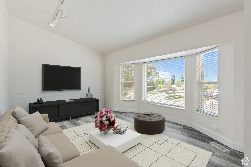 Living area featuring rail lighting, lofted ceiling, wood finished floors, and baseboards