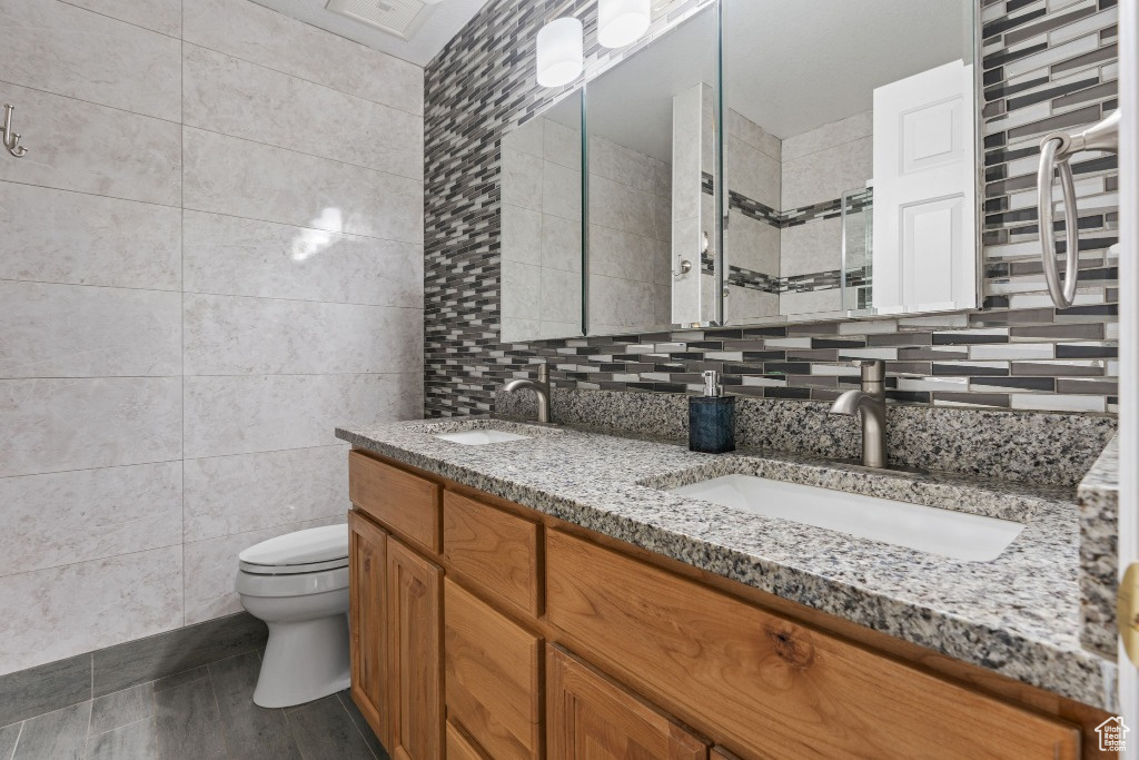 Full bathroom with tile walls, toilet, double vanity, a tile shower, and backsplash