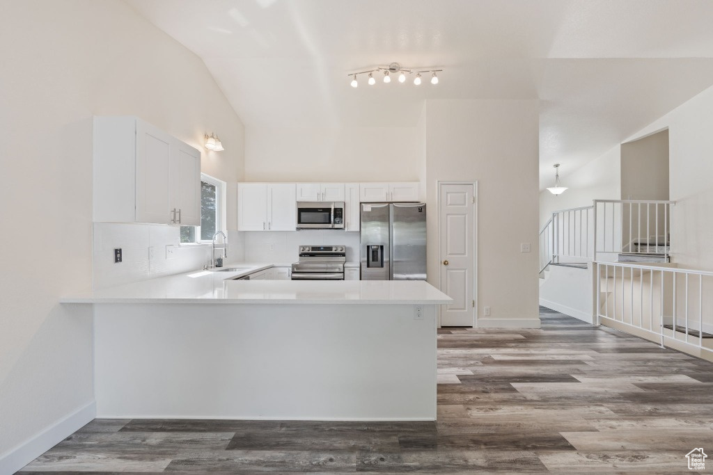 Kitchen featuring stainless steel appliances, a peninsula, light countertops, white cabinetry, and high vaulted ceiling