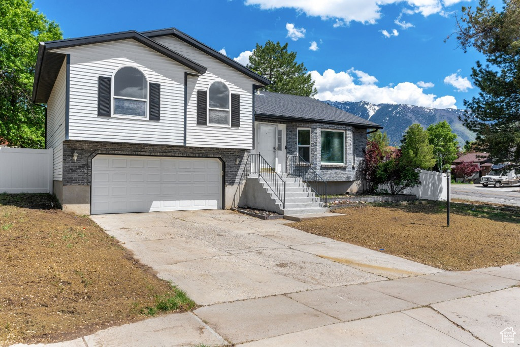 Split level home with an attached garage, driveway, fence, and a mountain view