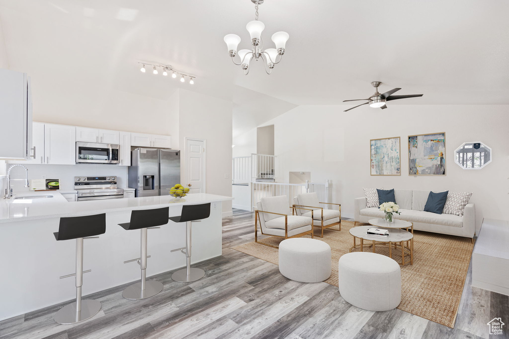 Living room featuring light wood-style floors, high vaulted ceiling, a ceiling fan, a chandelier, and rail lighting