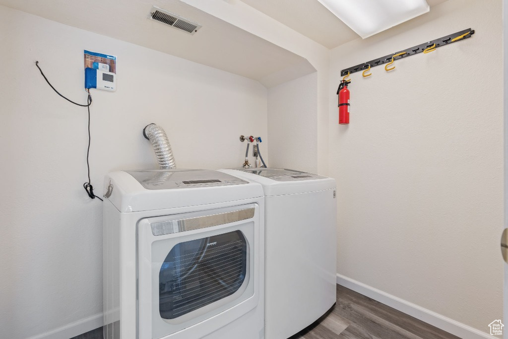 Clothes washing area featuring washing machine and dryer, baseboards, and wood finished floors