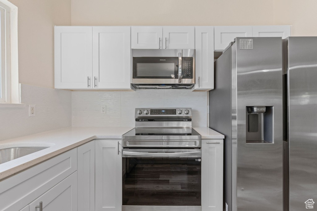Kitchen featuring stainless steel appliances, white cabinetry, light countertops, and backsplash