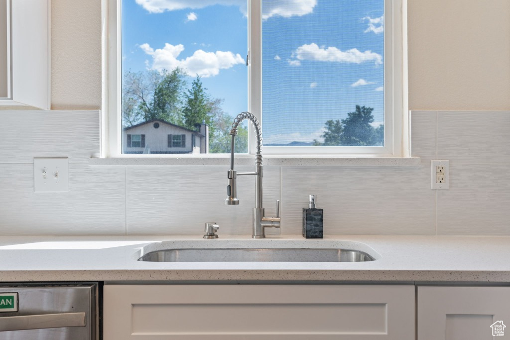 Kitchen view of a sink, stainless steel dishwasher, white cabinetry, tasteful backsplash, and light stone counters