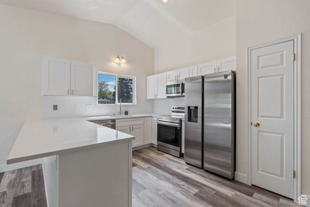 Kitchen with stainless steel appliances, a peninsula, white cabinets, light countertops, and light wood-style flooring