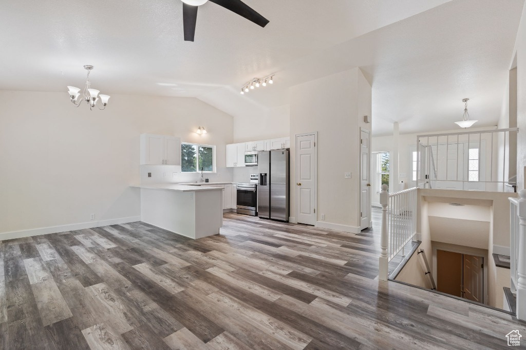 Kitchen featuring stainless steel appliances, a peninsula, white cabinetry, wood finished floors, and high vaulted ceiling