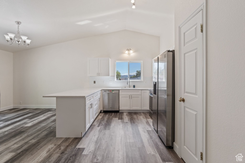 Kitchen with appliances with stainless steel finishes, a peninsula, dark wood-style flooring, white cabinetry, and lofted ceiling