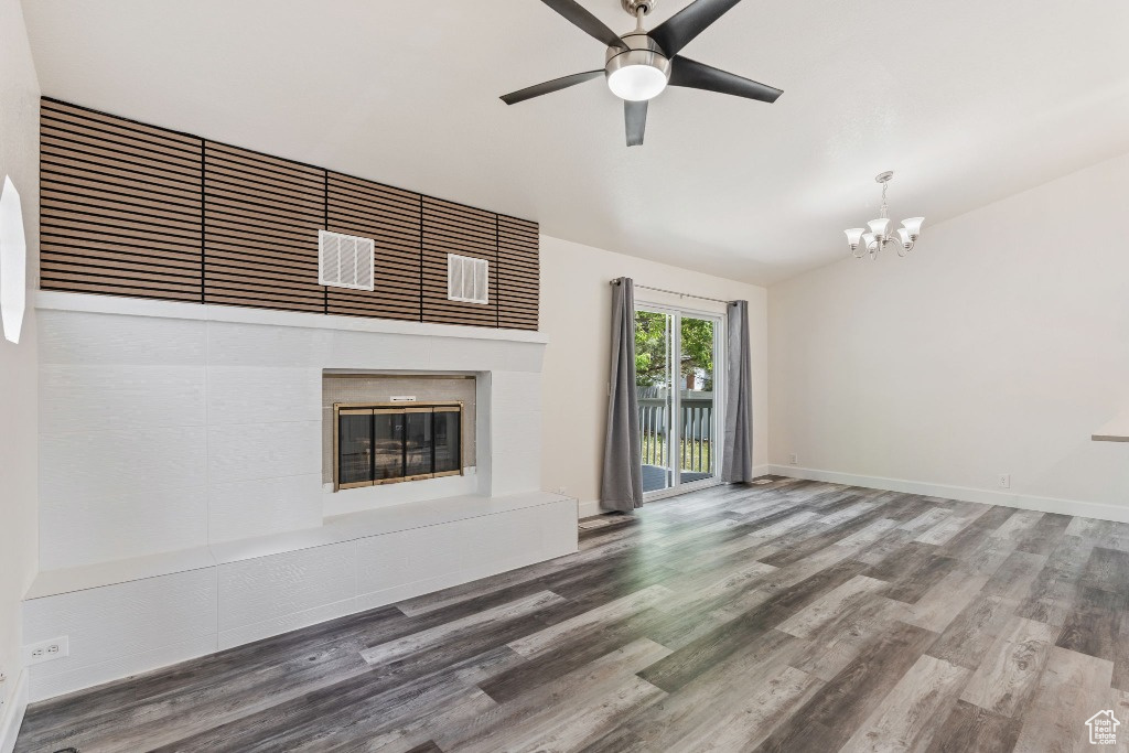 Unfurnished living room with a chandelier, a glass covered fireplace, lofted ceiling, wood finished floors, and ceiling fan