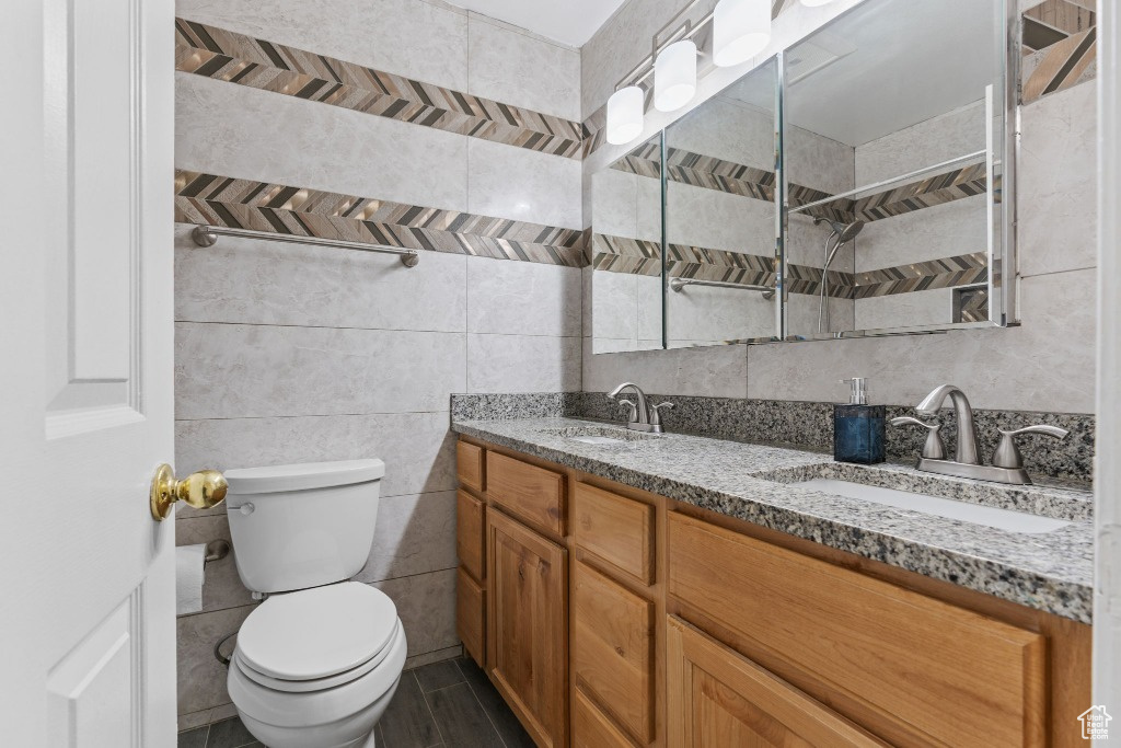 Bathroom featuring toilet, tile walls, double vanity, and a tile shower