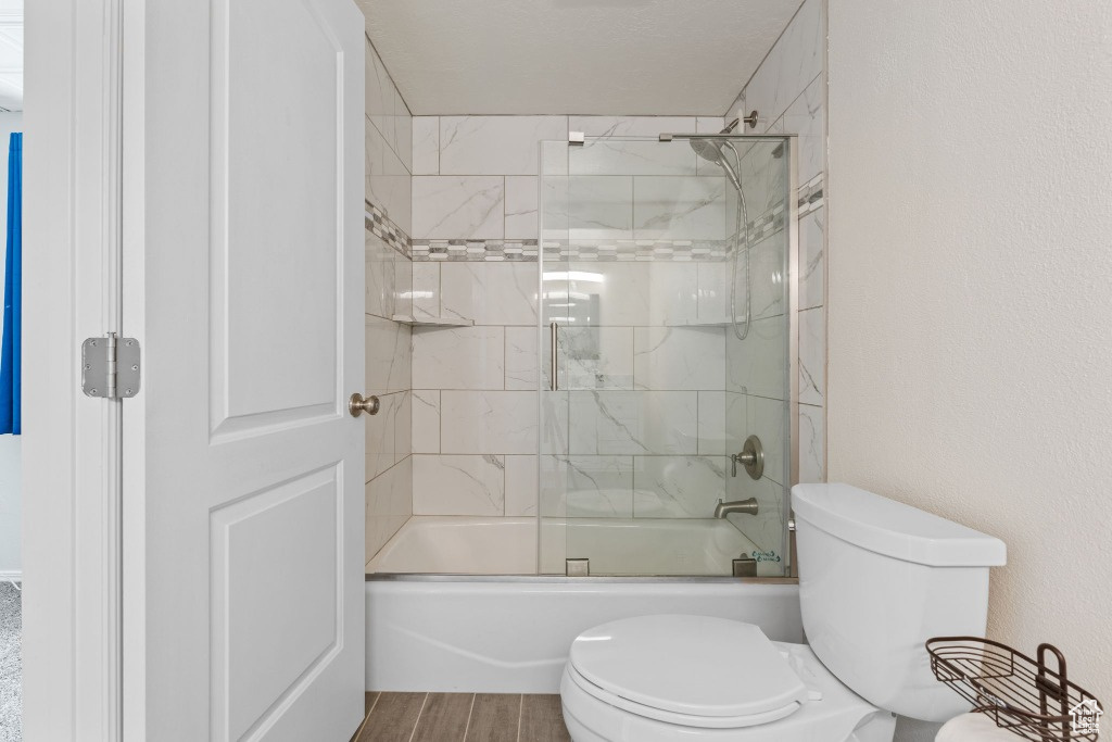 Full bath with toilet, shower / bath combination with glass door, and wood finished floors